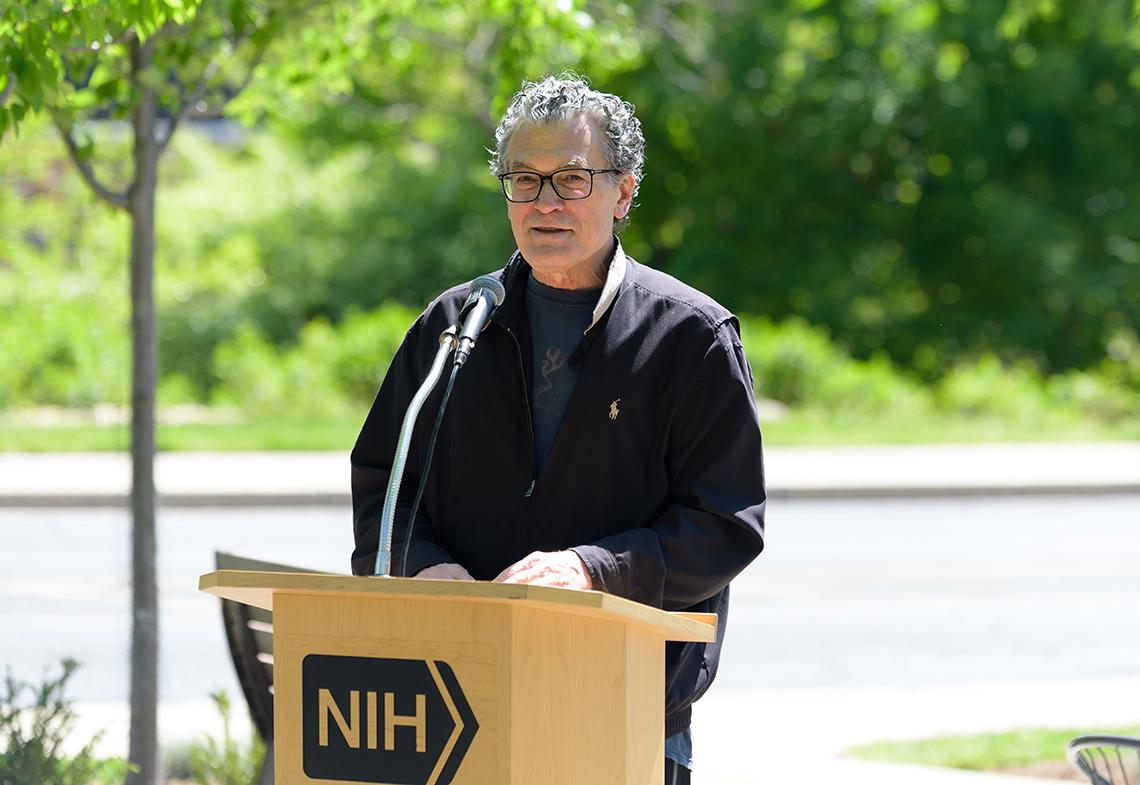 Perez-Stable stands speaking into microphone at podium outside.