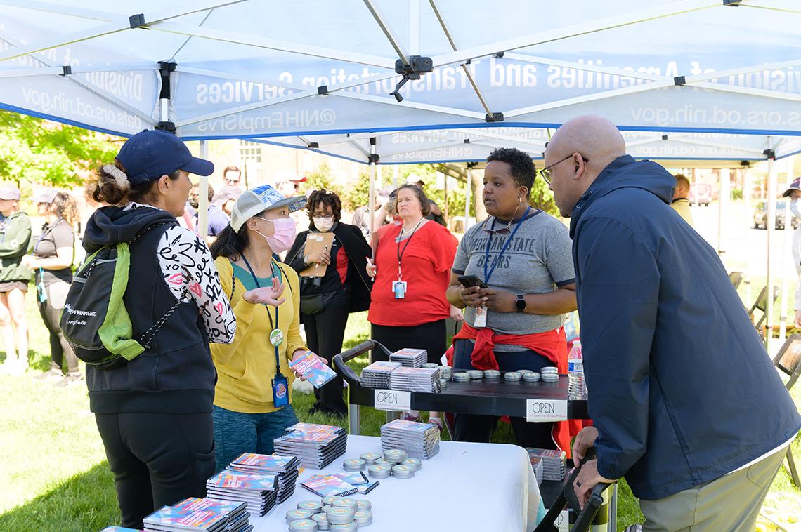 Exhibitors talk with runners at information tables outside under tent.