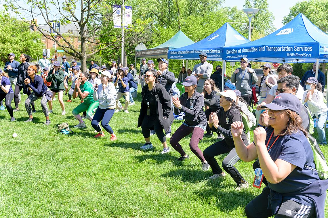 Dozens of runners squat during warmup exercises on the lawn.