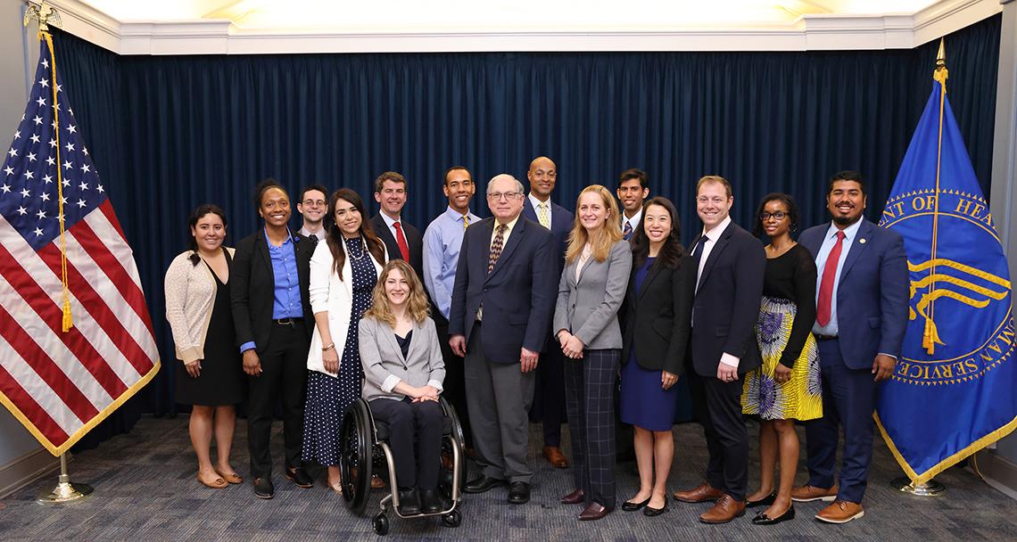 The group of fellows pose with Tabak, Schwetz next to U.S. and HHS flags.