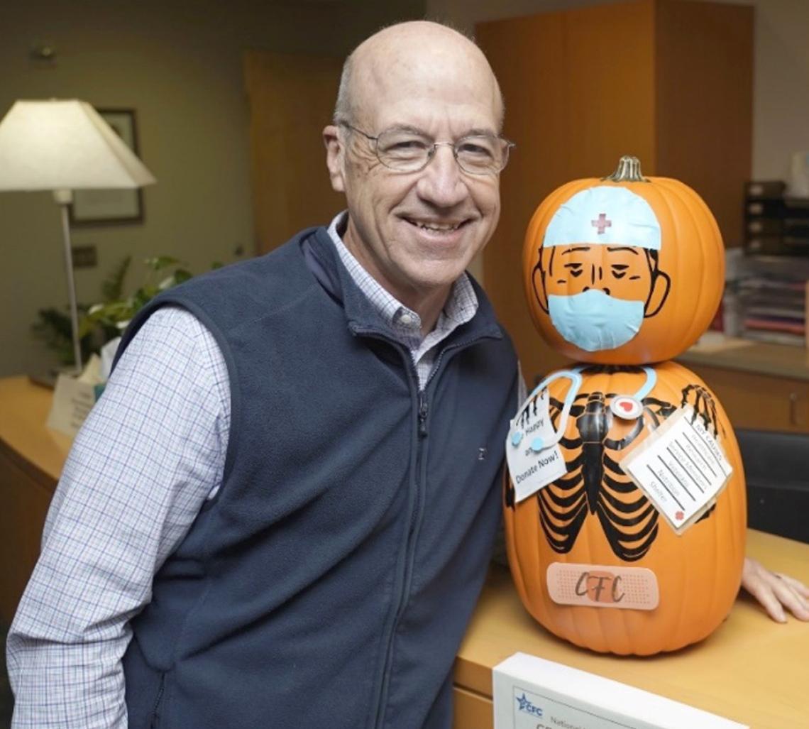Gilman beside two stacked pumpkins wearing surgeon's mask and cap, painted with a black skeleton torso