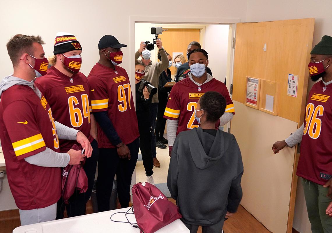 Young person in gray hoodie with back to camera greets five guys in face masks and football jerseys.