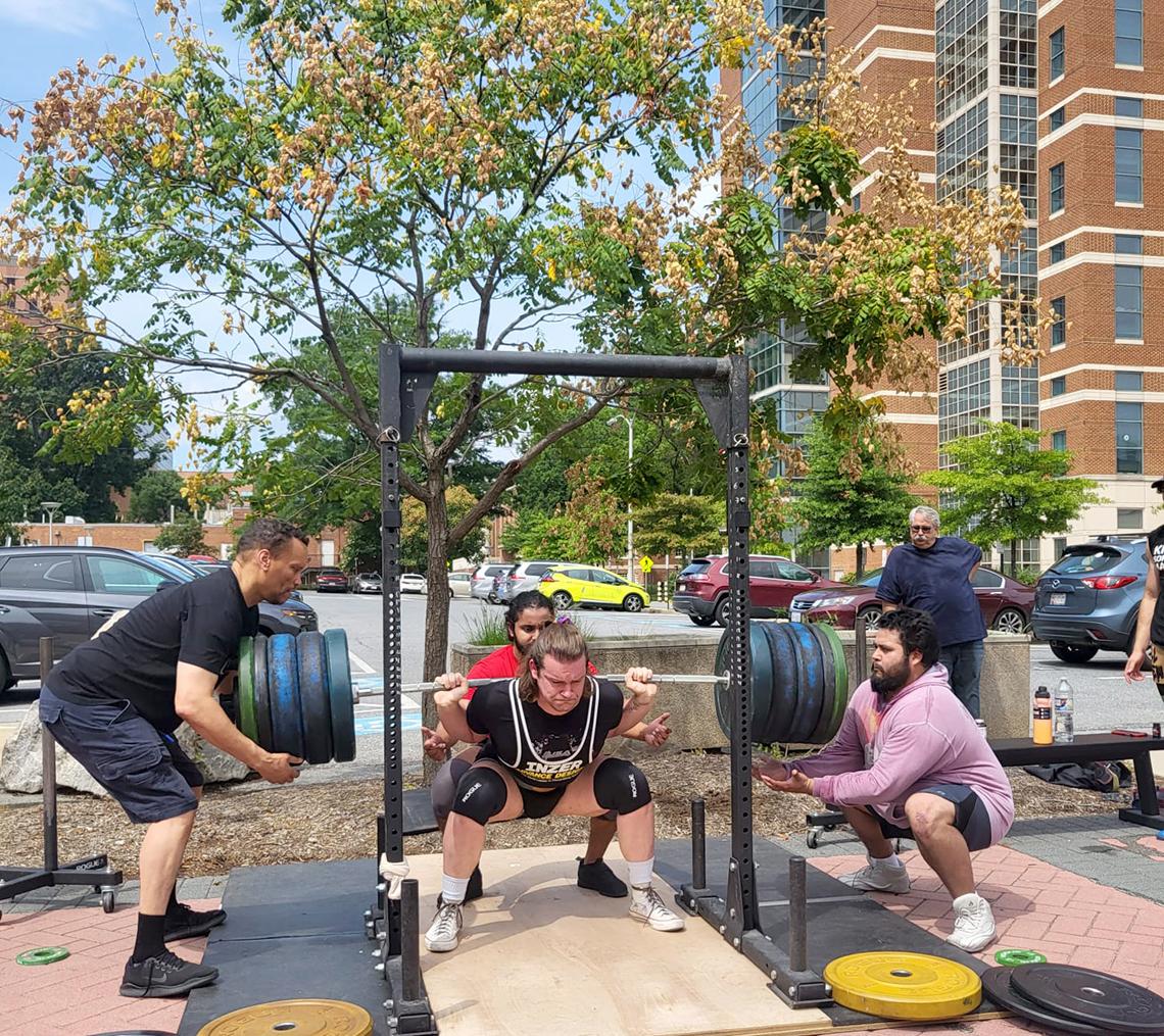 Two men spot Lowe as he performs a squat