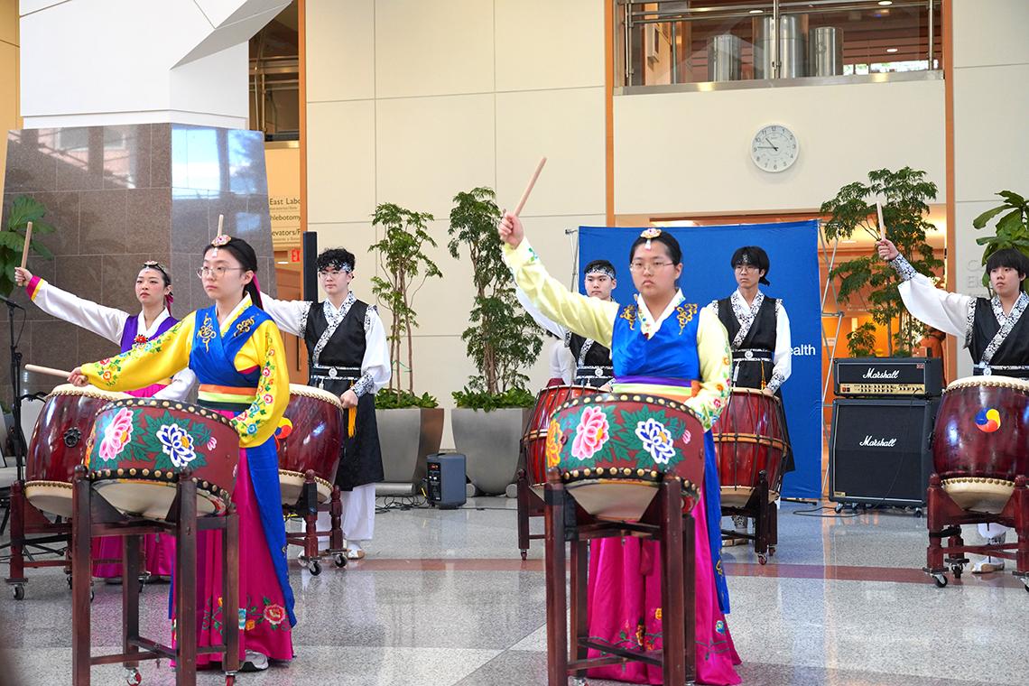 Students in traditional dress play large, elaborately decorated drums.