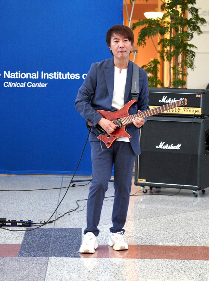 Man in a dark blue suit and white shirt plays an electric guitar.