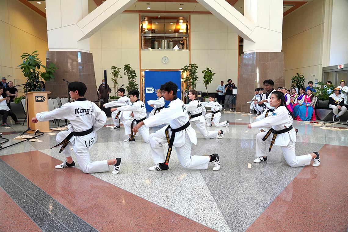 Taekwondo students kneel mid-action during a demonstration. They wear white uniforms with black belts.