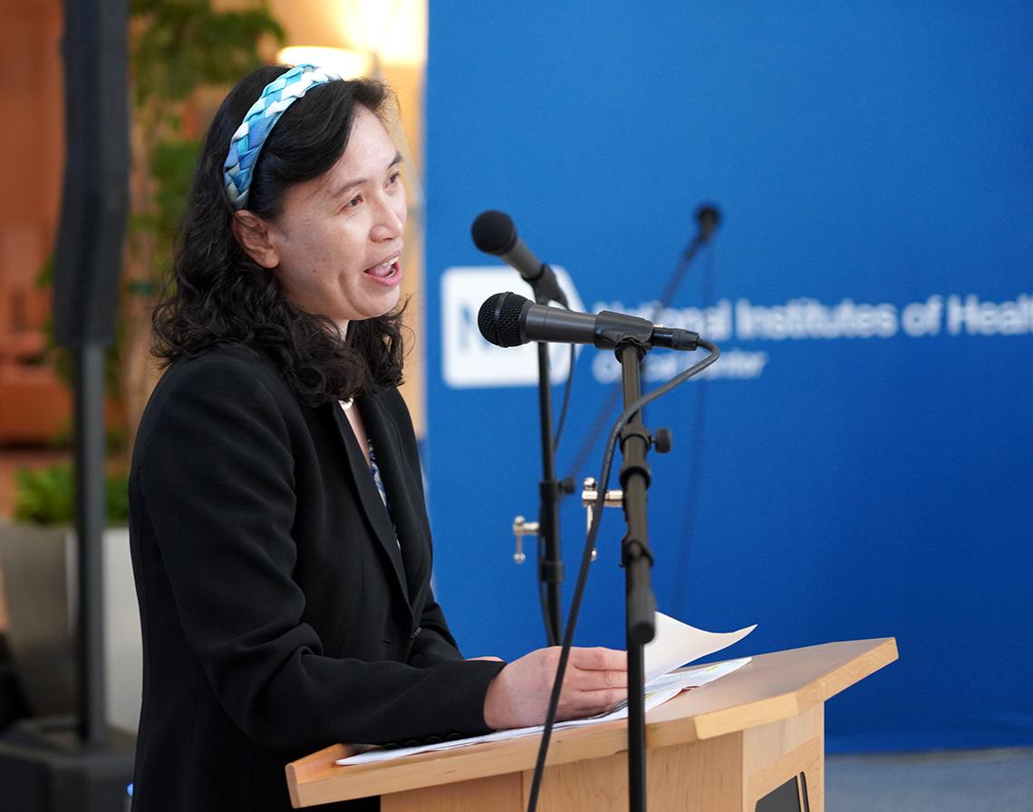 Dark-haired woman speaks into a microphone mounted on a podium.