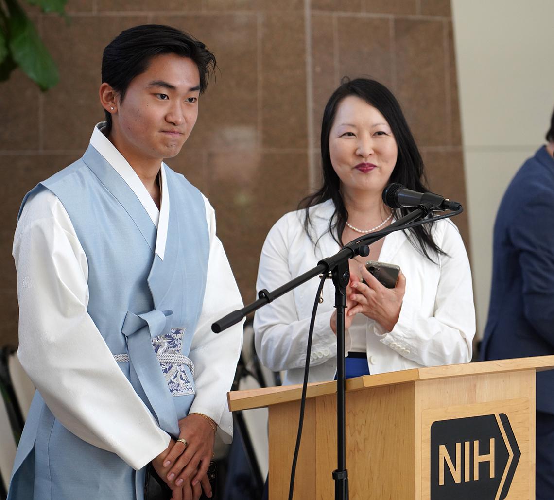 Male and female speakers stand back from a podium as they listen to an audience member speak off-camera.