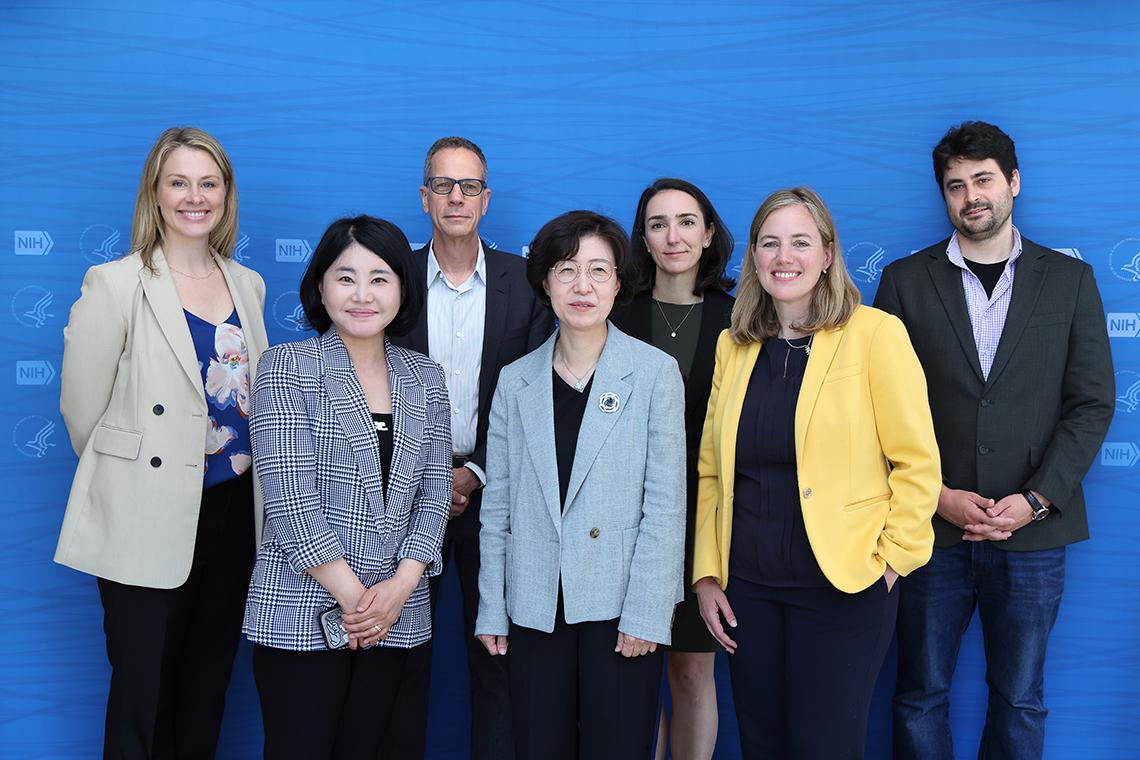 The Korean delegates pose with VRC staff against a blue backdrop bearing the NIH logo.