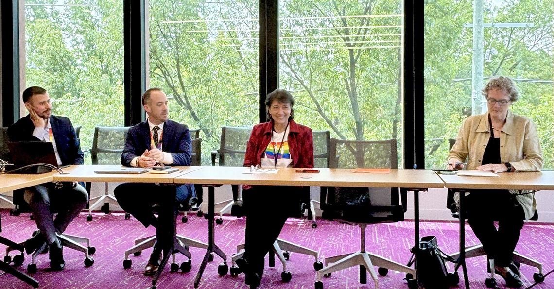 Bertagnolli and Marrazzo seated at a long table with representatives from Whitman-Walker. The room has bright purple carpet and floor-to-ceiling windows.