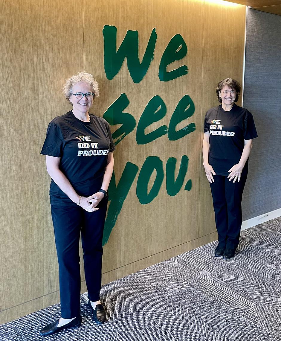 Marrazzo and Bertagnolli pose against a wall bearing a large display that reads "We See You."