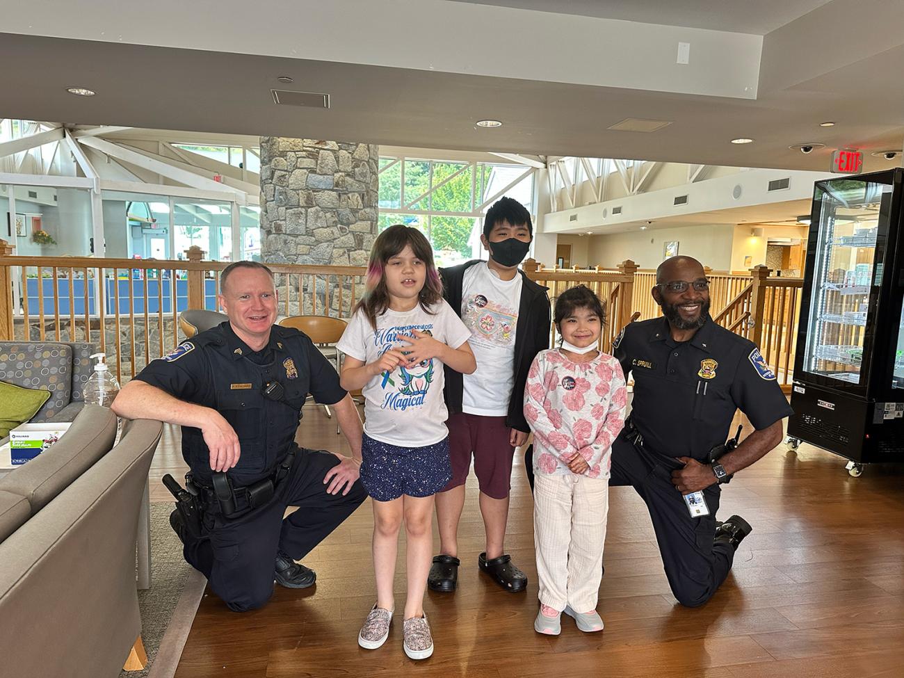 Two police officers kneel on either side of a group of three young children.