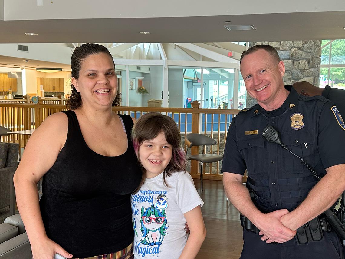 A mother and young child embrace next to a uniformed police officer.