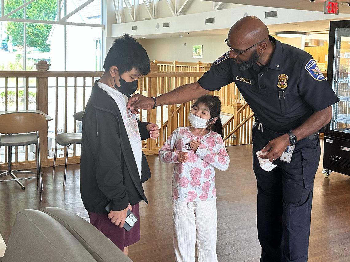 A uniformed police officer stoops to place a sticker on the shirt of a masked patient. Another patient looks on.