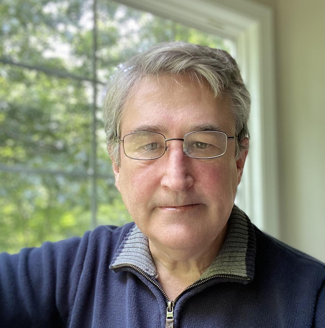 Headshot of Schmitt, who is standing against a window with a forested view.