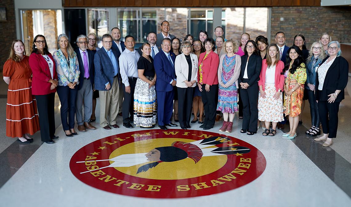 NIH'ers and members of the Native tribe assemble, large red and yellow Absentee Shawnee Tribe logo on floor