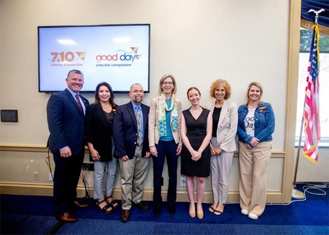 NIH'ers and Good Days representatives pose for a photo in front of a projector screen.