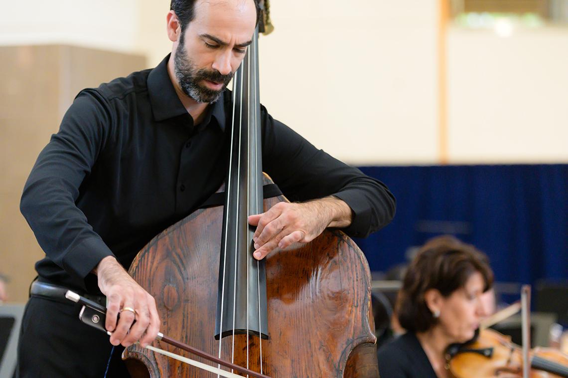 A man holds double bass, gliding his bow across it.