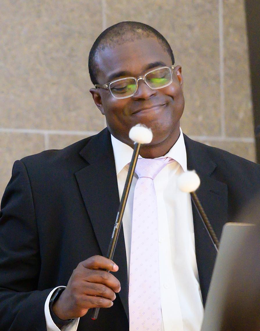 A man smiles as he holds up his timpani mallets.