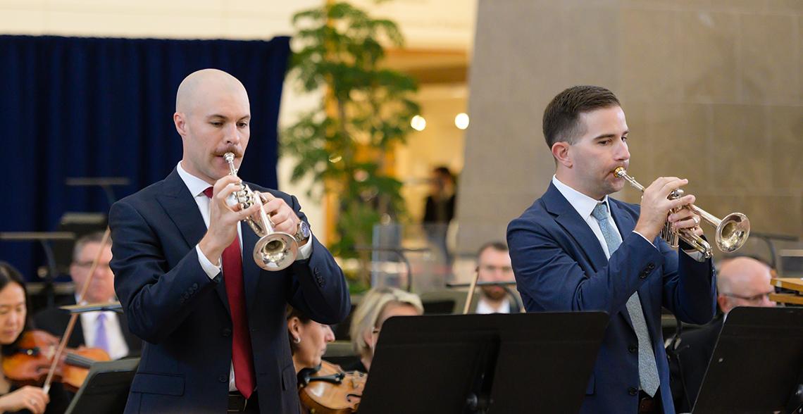 Two men hold smaller "piccolo trumpets" to their lips.
