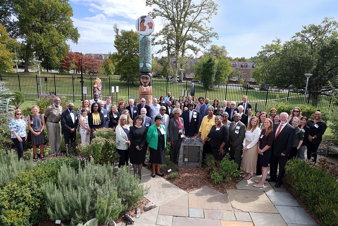 Attendees gather for a group photo behind the plaque