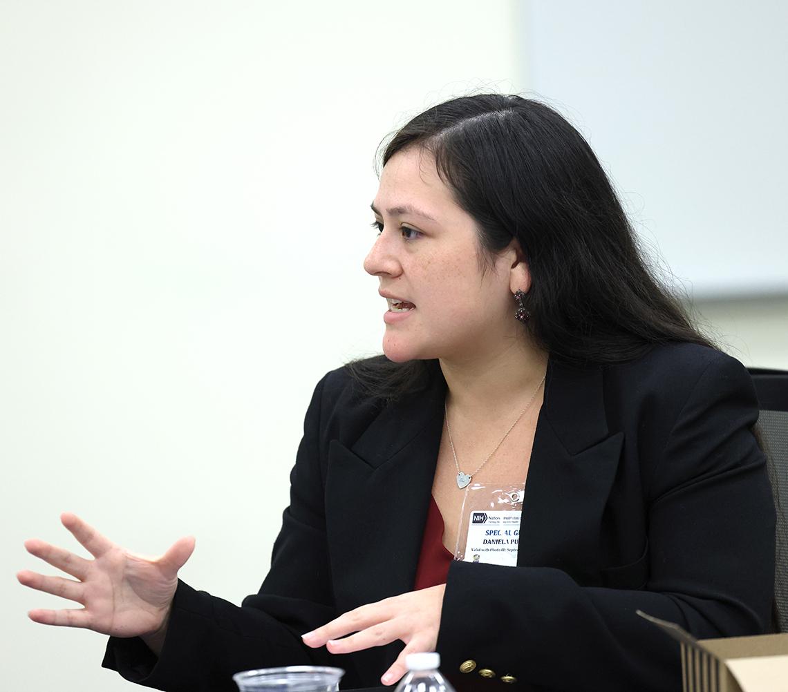 A woman talks, side view, with hands extended.