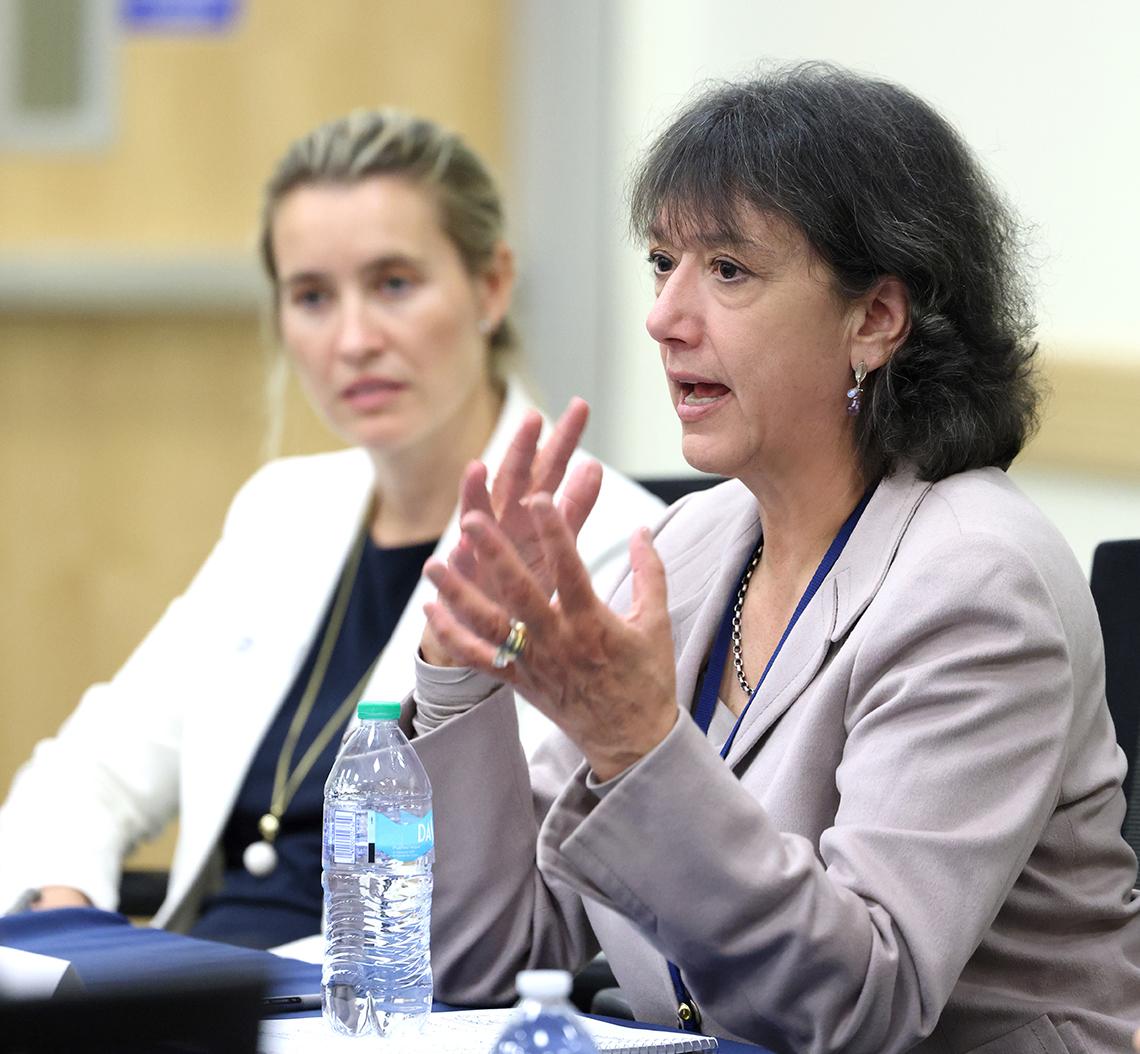 Bertagnolli, elbows on table, hands together talks, while Klimczak looks on.