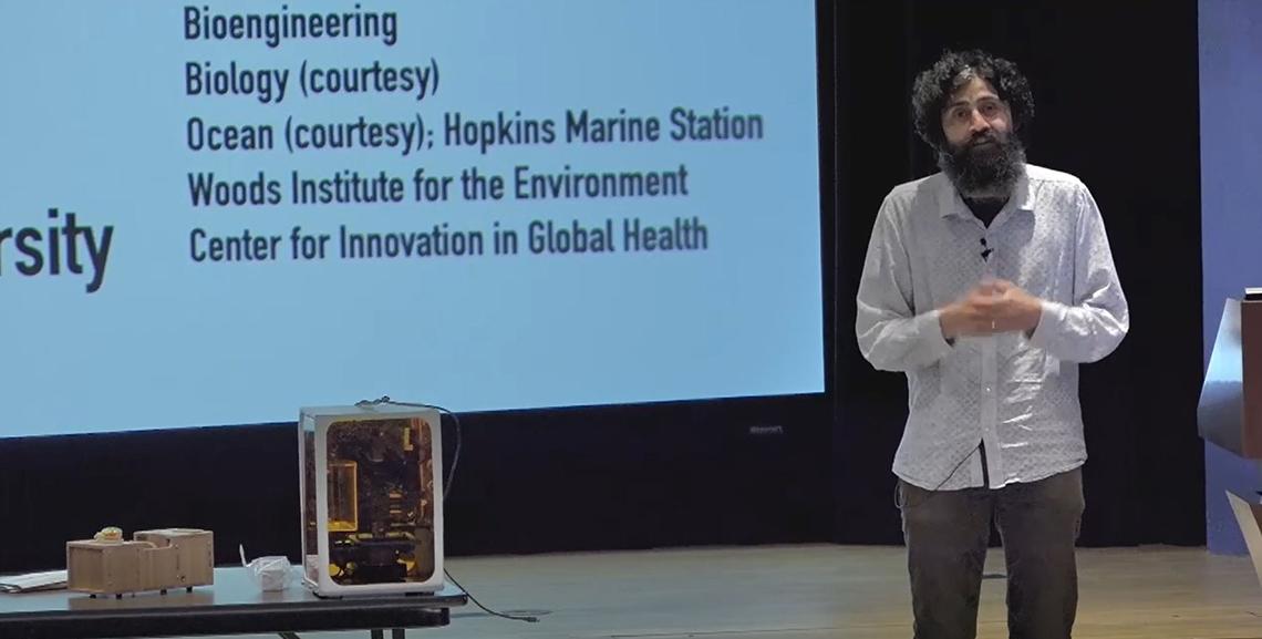 Dr. Prakash stands on stage next two devices