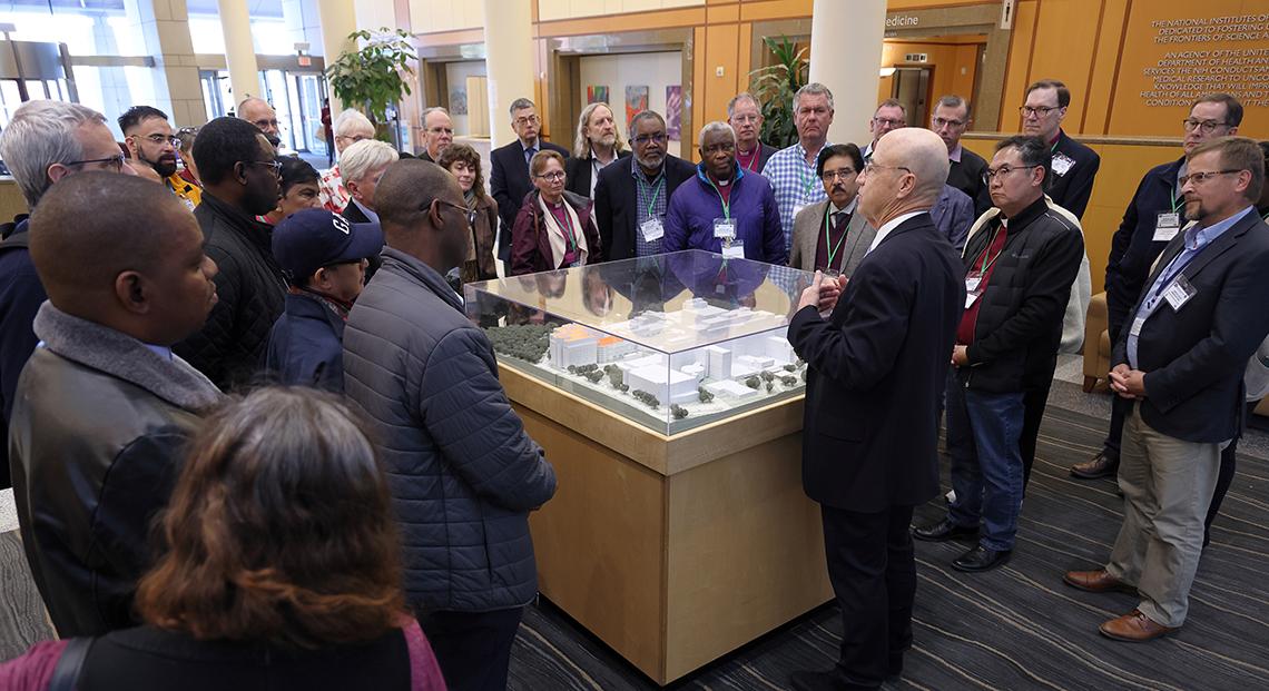 Gilman stands talking with the group standing all around the CC model in the atrium.