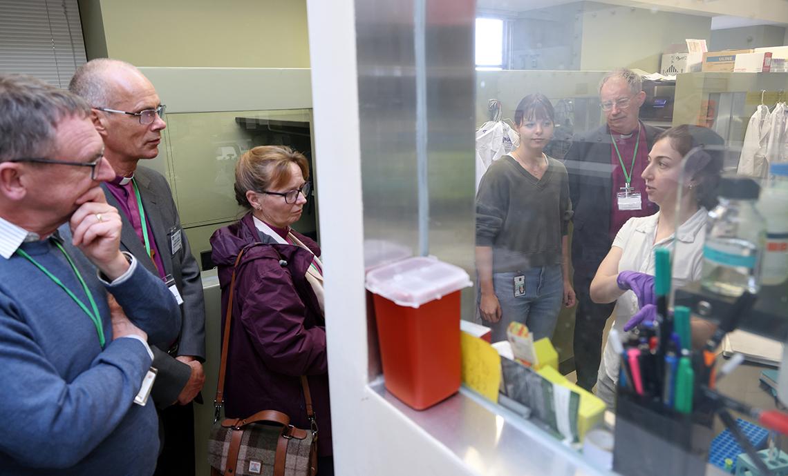 Several people stand peering around a wall into a lab.