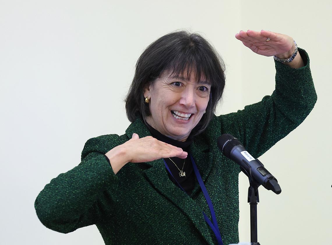 Bertagnolli in green dress talks with hands framed around her face.