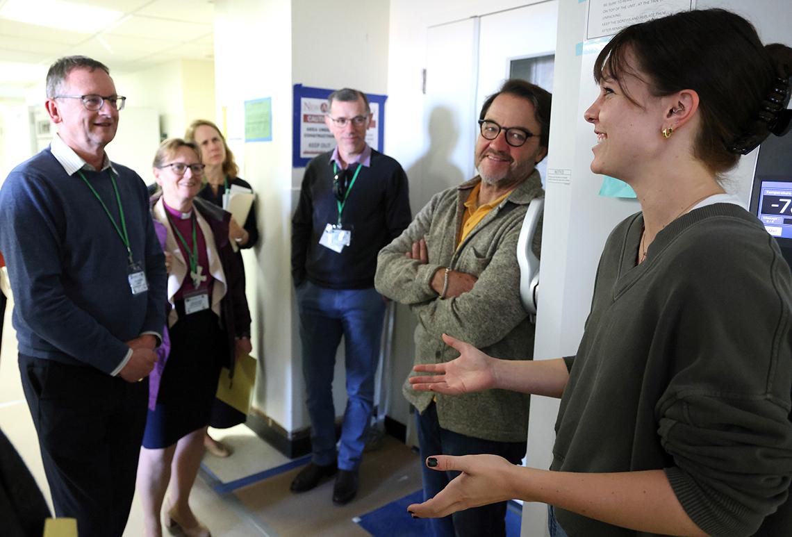 In hallway, woman talks as Tisdale and visitors listen.