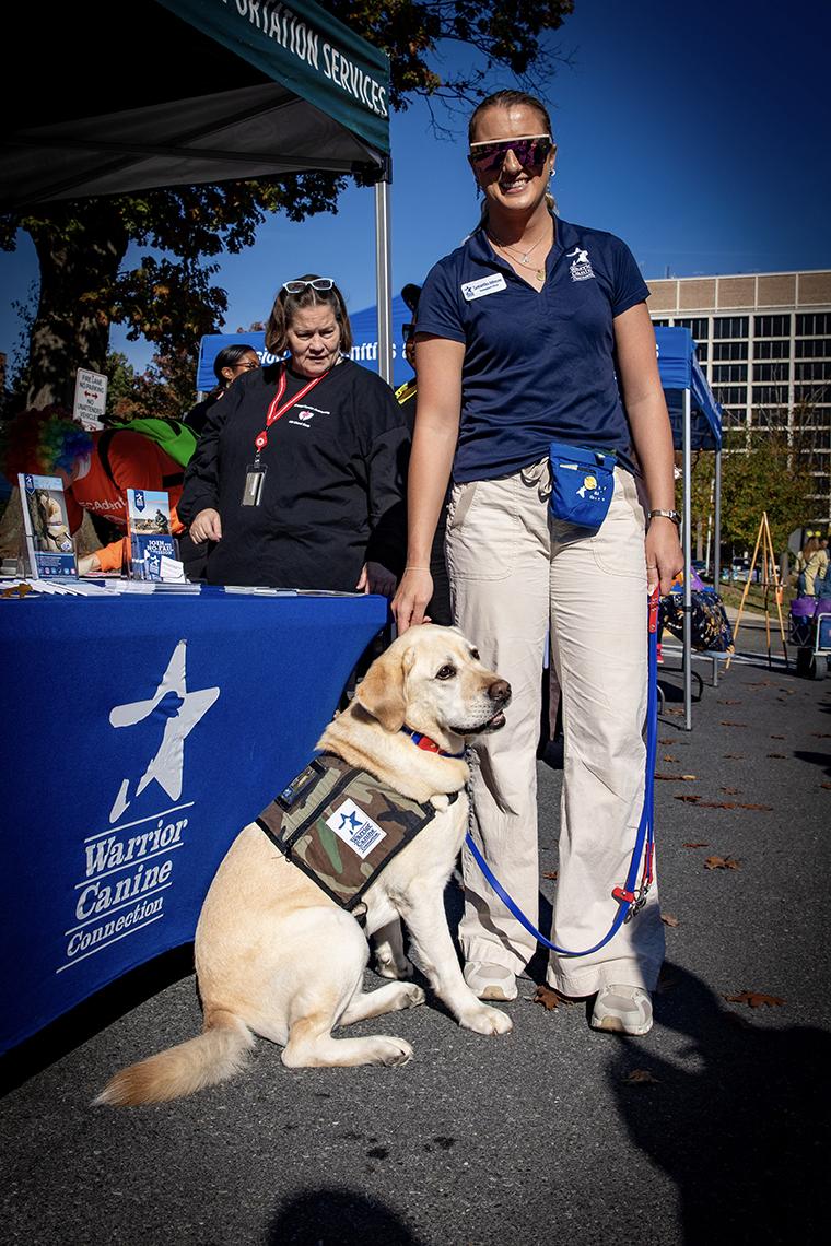 A woman in a navy polo and tan pants poses with a yellow Labrador. 