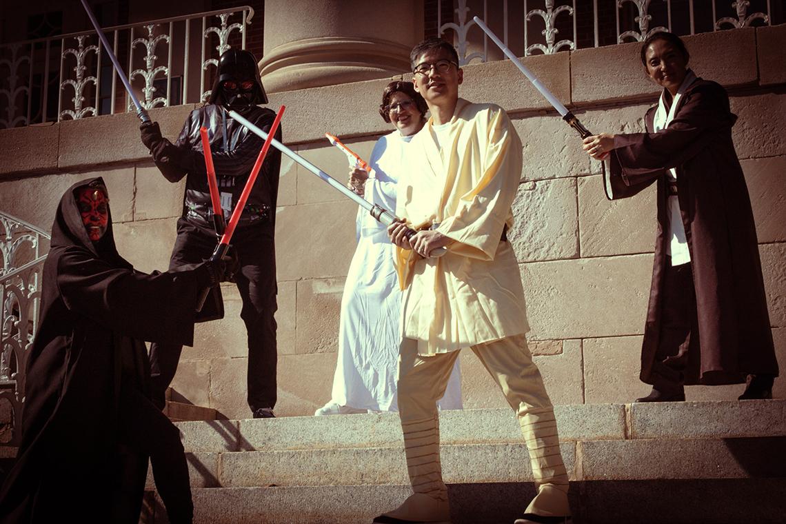 Five NIH'ers in Star Wars garb pose with lightsabers and blasters on the steps of a building.