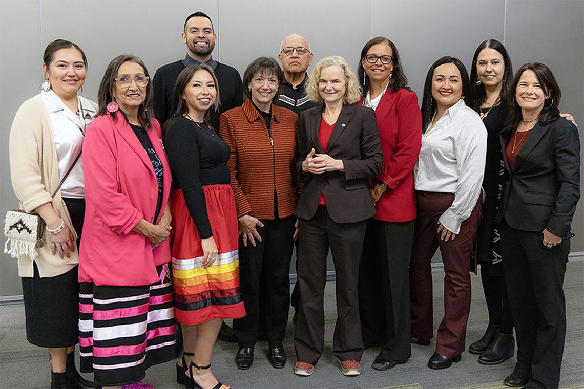 A group poses for a photo. Some of the individuals wear wear tribal-inspired clothing or accessories.