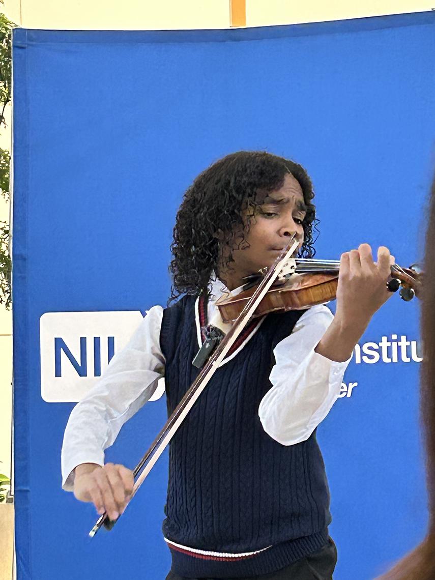 Sant plays the violin against a blue NIH backdrop.