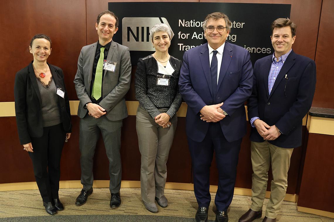 Group photo in front of red wall, NCATS sign