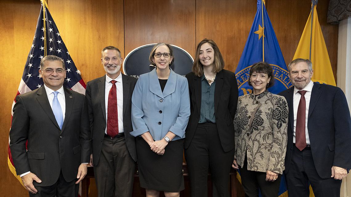 Group photo at swearing-in, next to U.S. and HHS flags
