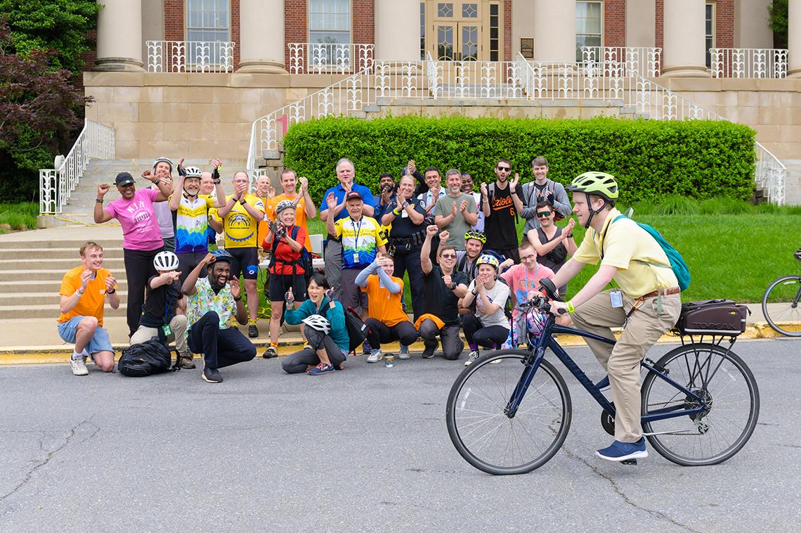 A cyclist rides past a crowd of cheering people in front of Bldg. 1