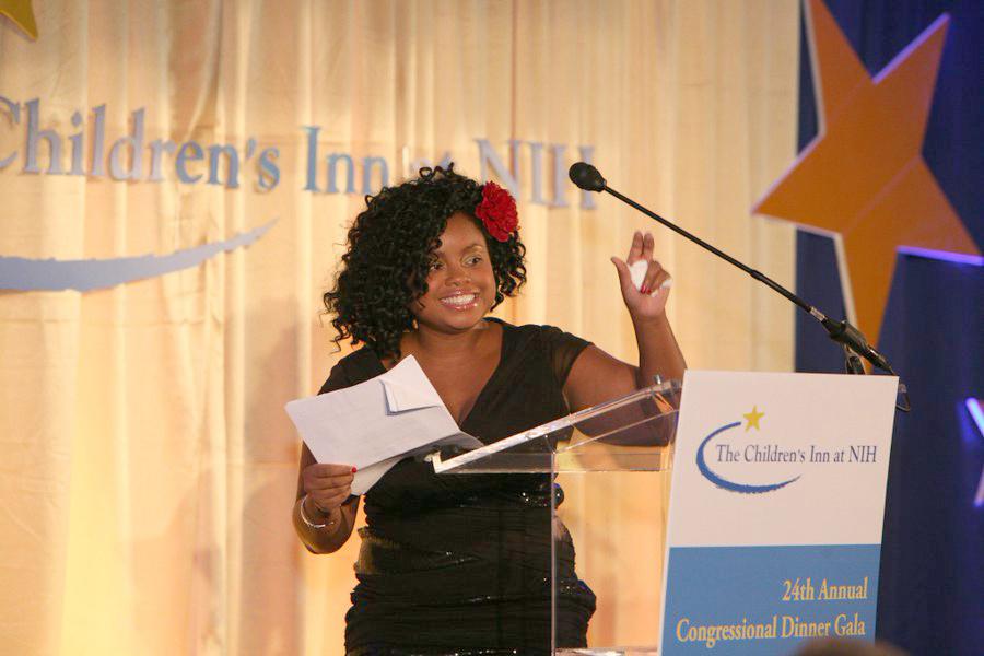An adult Broadbent waves to the audience as she steps back from a speaker's podium.