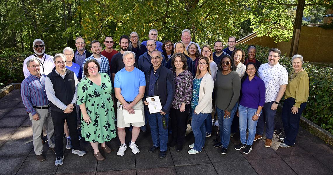Large group of people standing together outside under trees