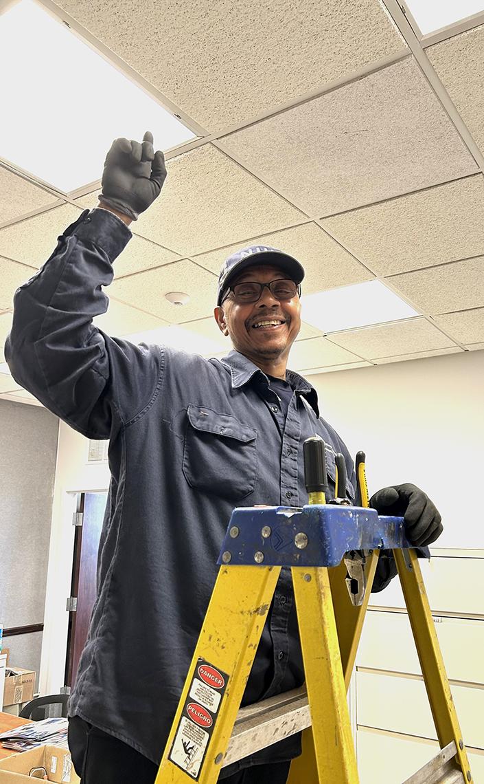 Hoes stands on ladder smiling, pointing to the lights, which now work.