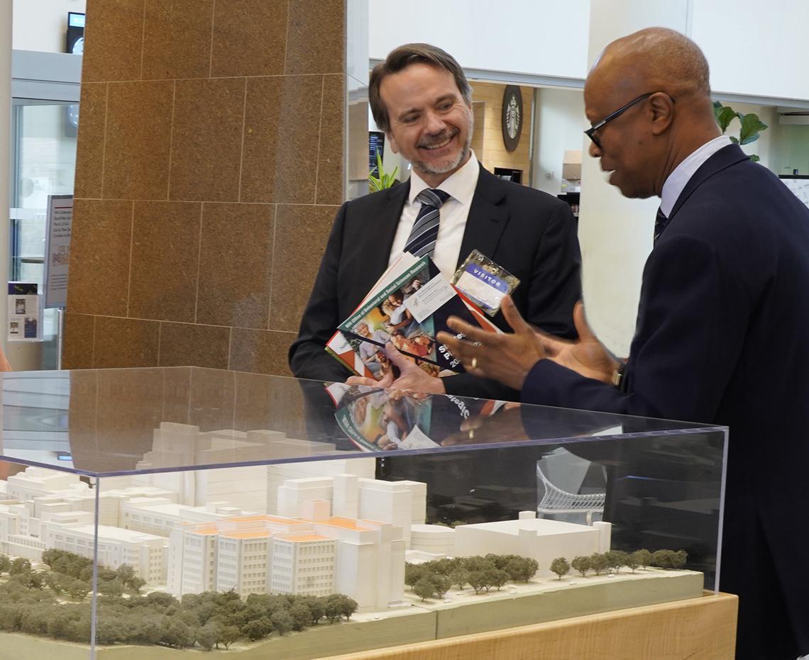 Aiyelawo (r) greets an HHS official at the building model in the CC atrium.
