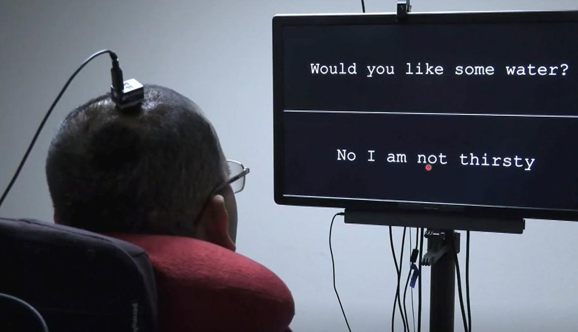 A man with a wire attached to his head watches a screen with the words "Would you like some water?" and "No, I am not thirsty"