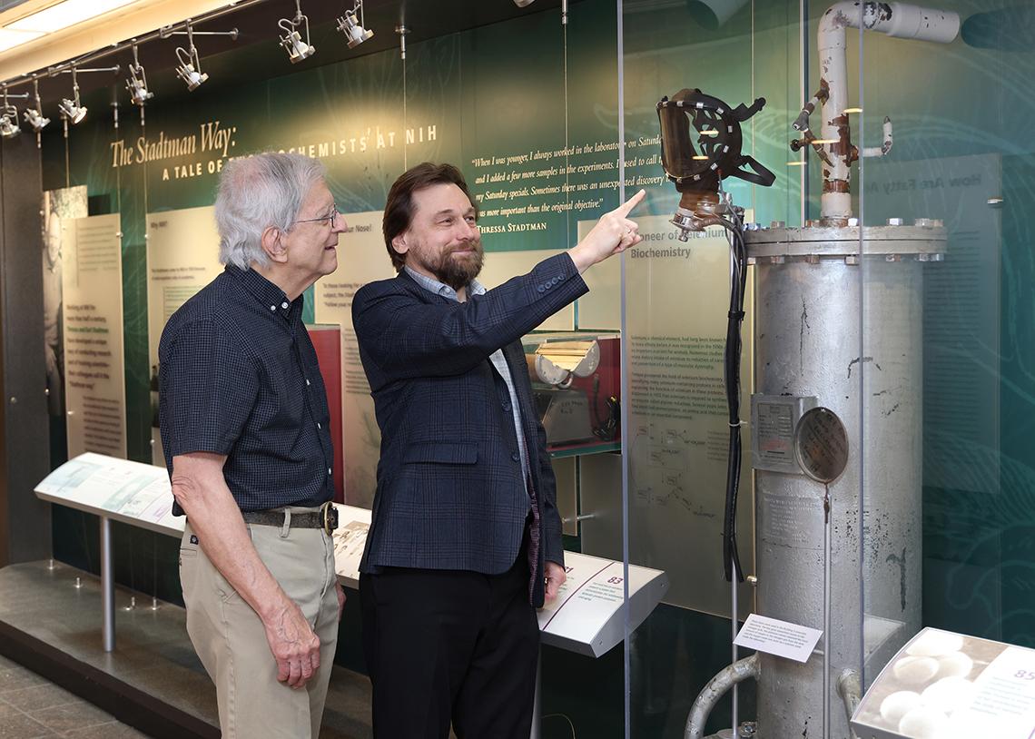 Gladyshev points to a mask in a Clinical Center display case as Dr. Richard Hodes looks on.