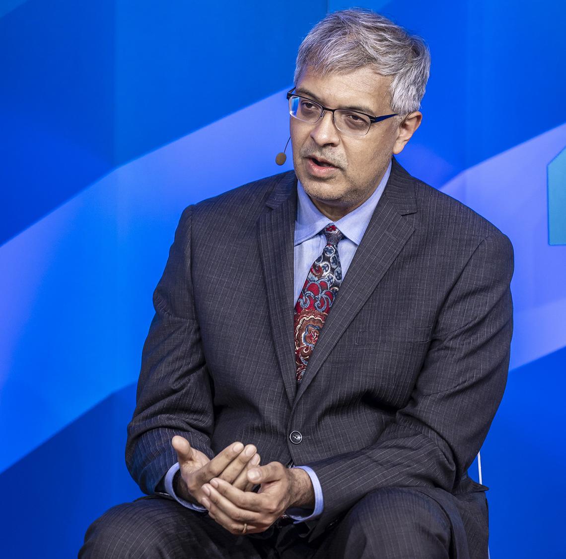 Dr. Jay Bhattacharya seated on stage with bright blue background