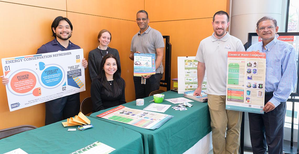 Colleagues hold energy conservation posters at table.