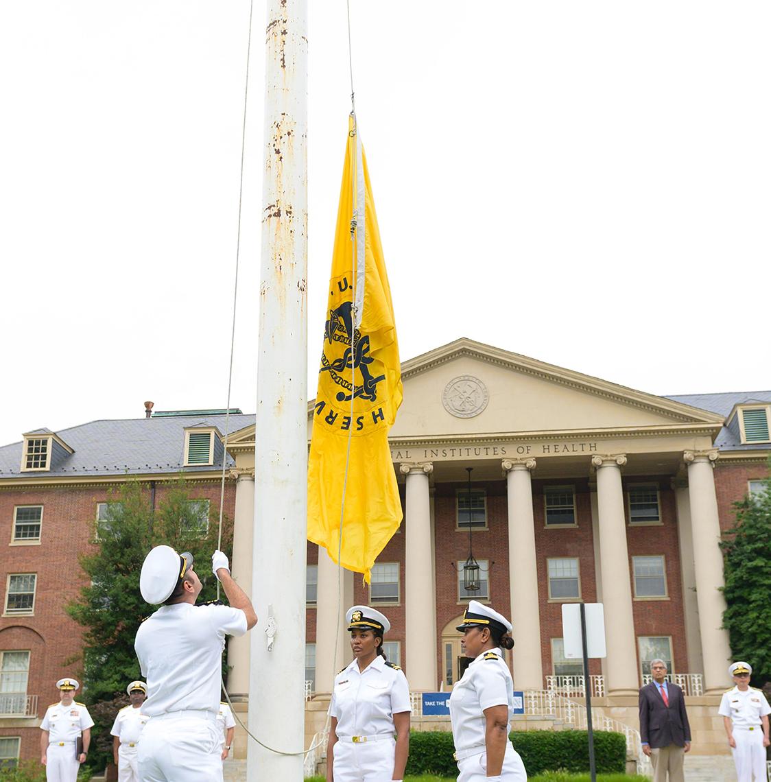 Three PHS members raise the USPHS flag in front of Bldg. 1.