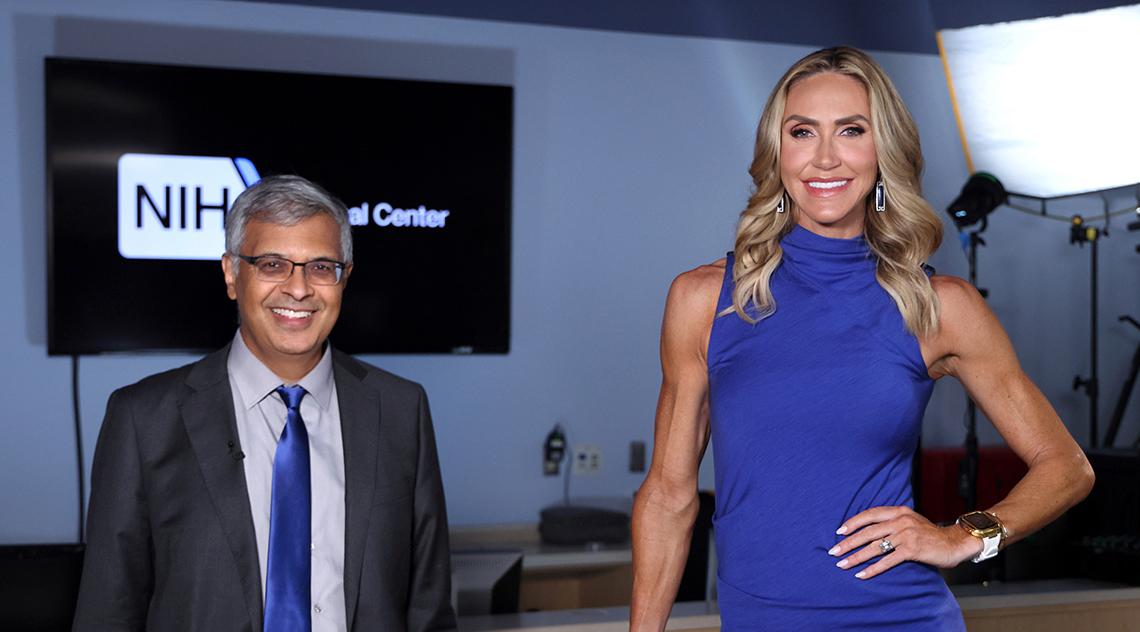 Lara Trump in blue dress stands on platform next to Bhattacharya near studio