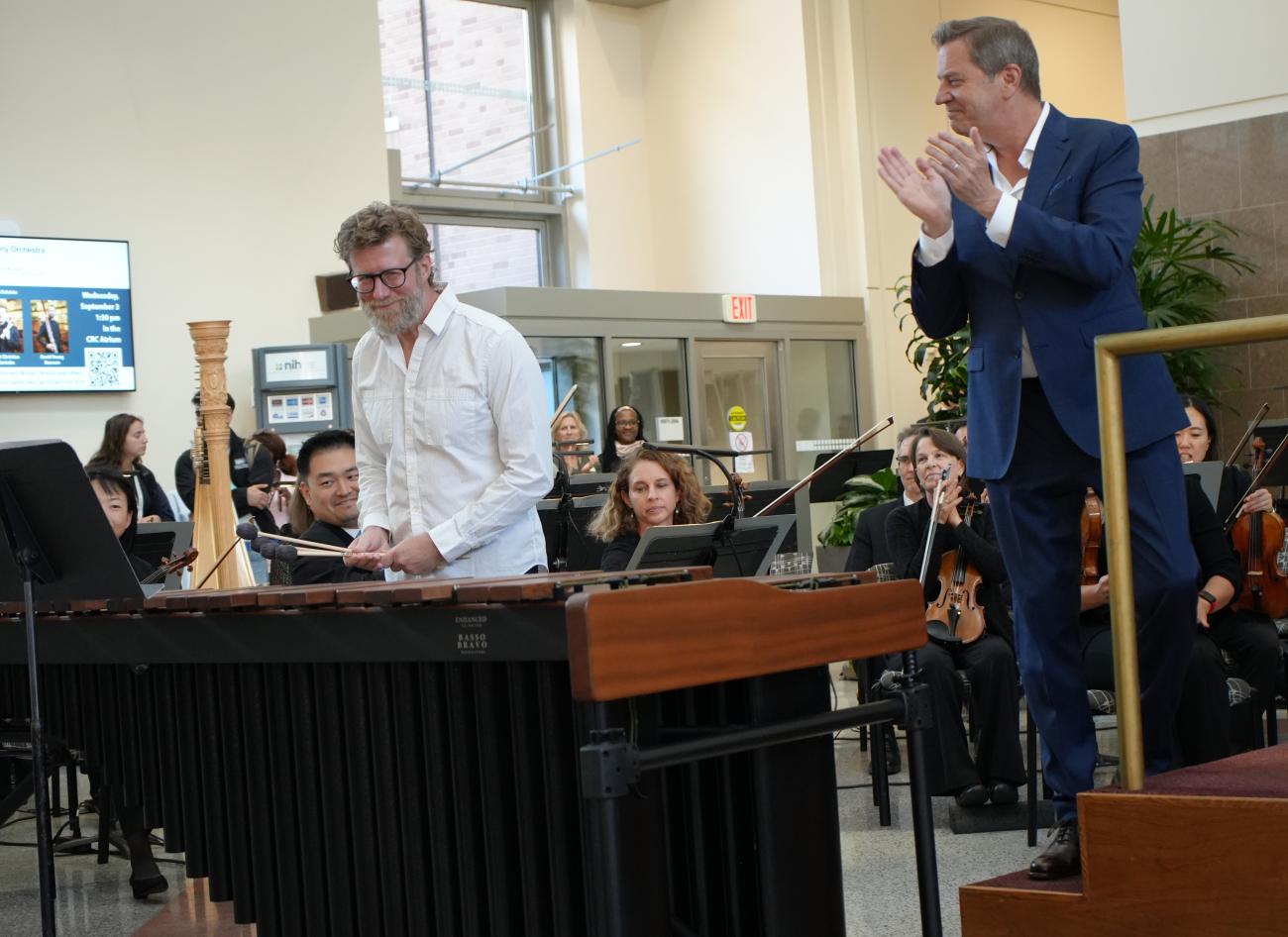 Smiling man holds 4 mallets over the marimba as the conductor applauds.